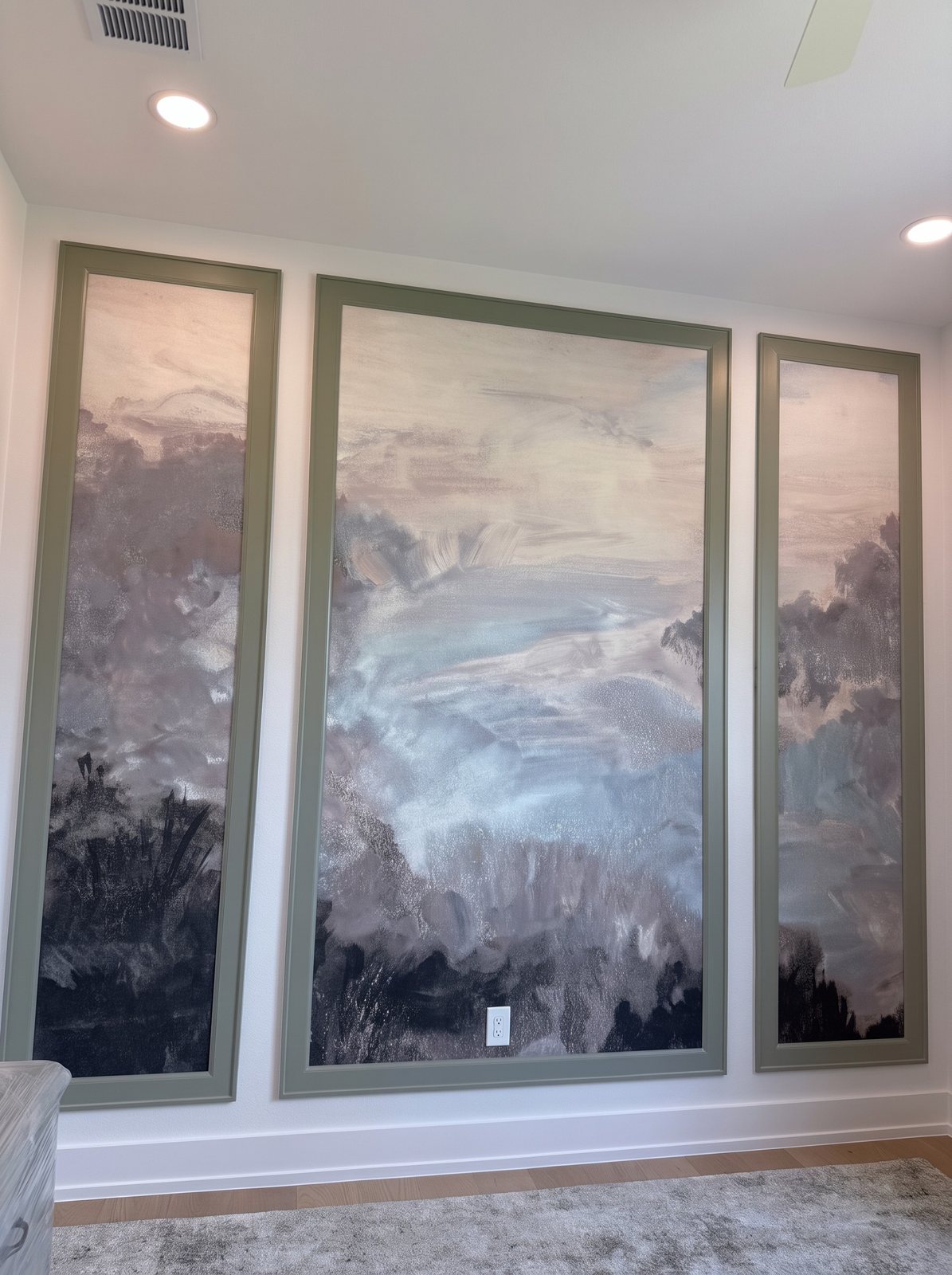 Wall with three sage-green picture-frame mouldings, each filled with part of one misty grey-blue landscape mural.