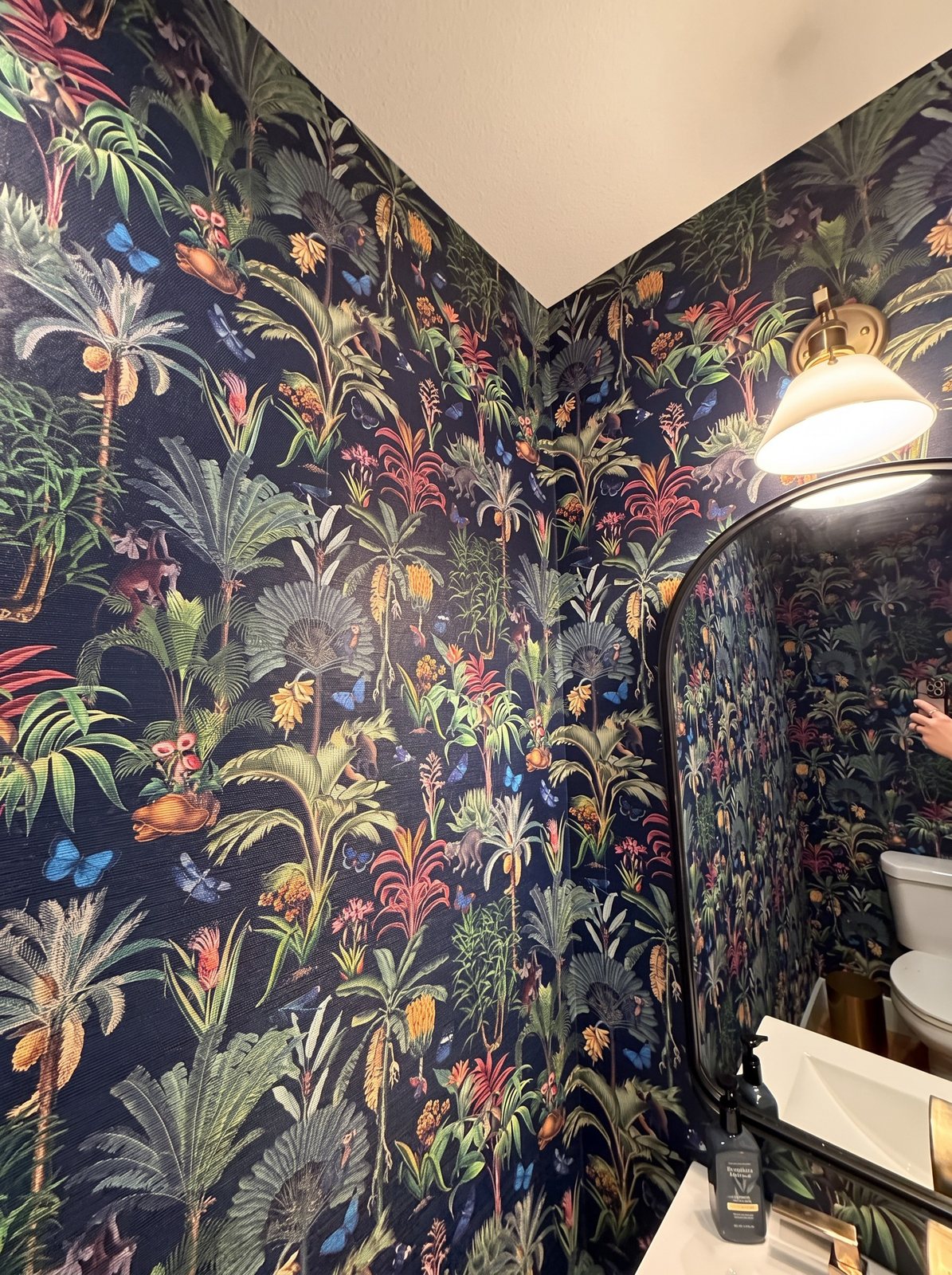 Powder room with dark navy tropical wallpaper of palms, flowers, monkeys and blue butterflies around an arched mirror.